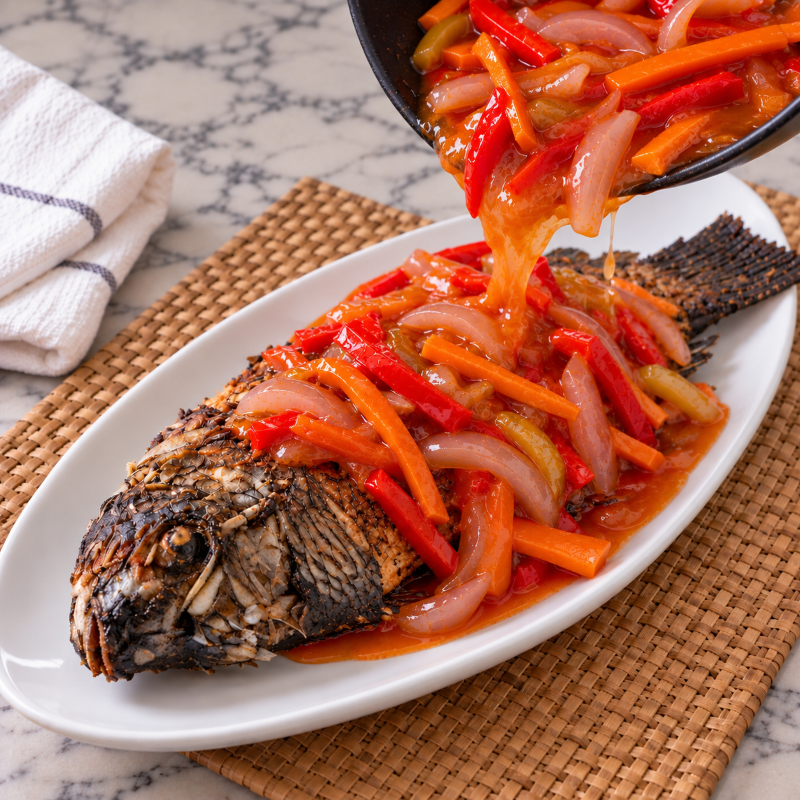 Escabecheng tilapia on a white dish with sweet and sour sauce being poured over.